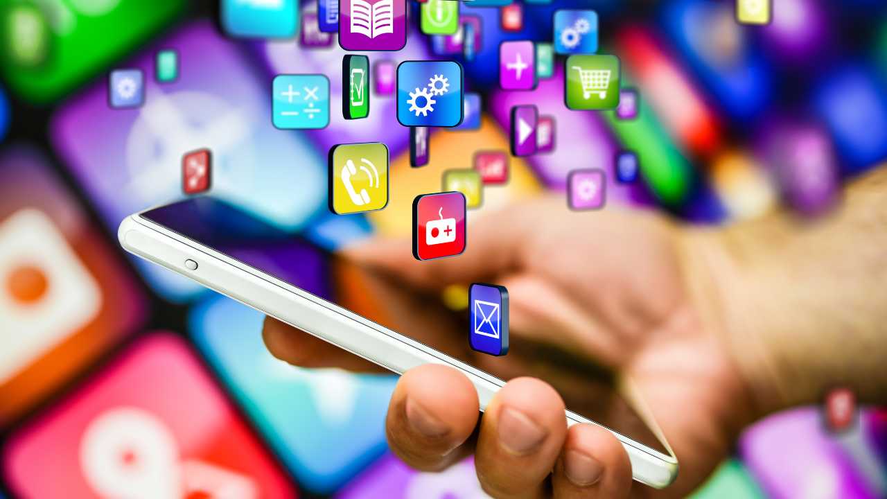 Uma mão humana segurando um celular com vários aplicativos voando em frente a tela.