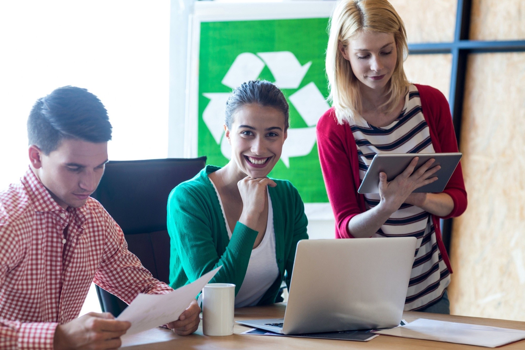 Equipe reunida em uma mesa com o símbolo da reciclagem ao fundo.