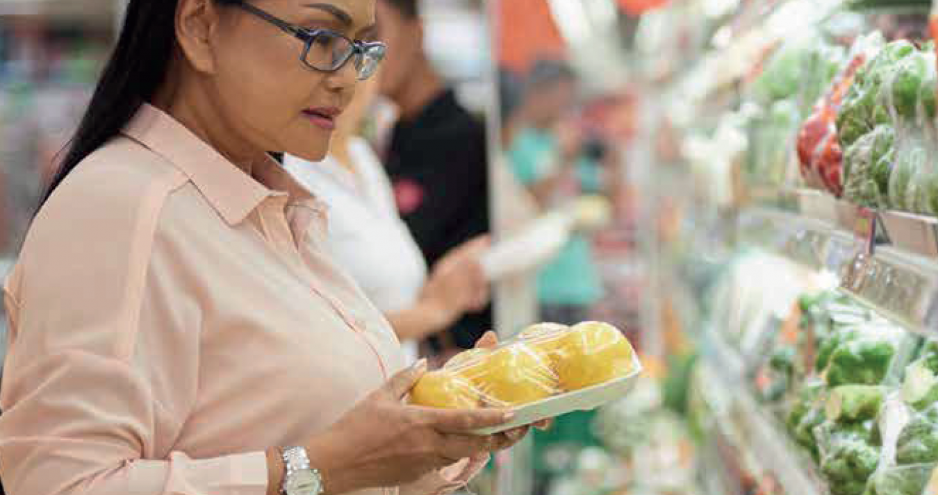 Mulher em uma secção de um super mercado segurando um tablete com frutas selecionadas.
