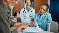 Enfermeira jovem ajudando um idoso a preencher documentos médicos na recepção do consultório médico