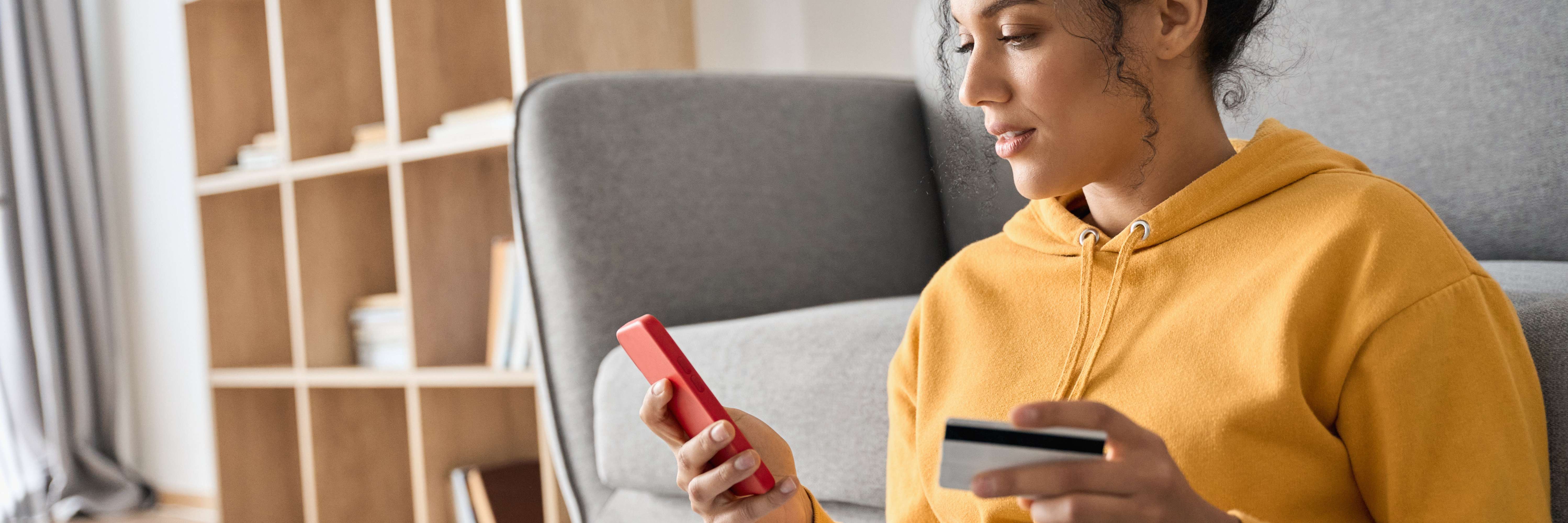 Mulher acessando o celular e com o cartão de crédito na outra mão.