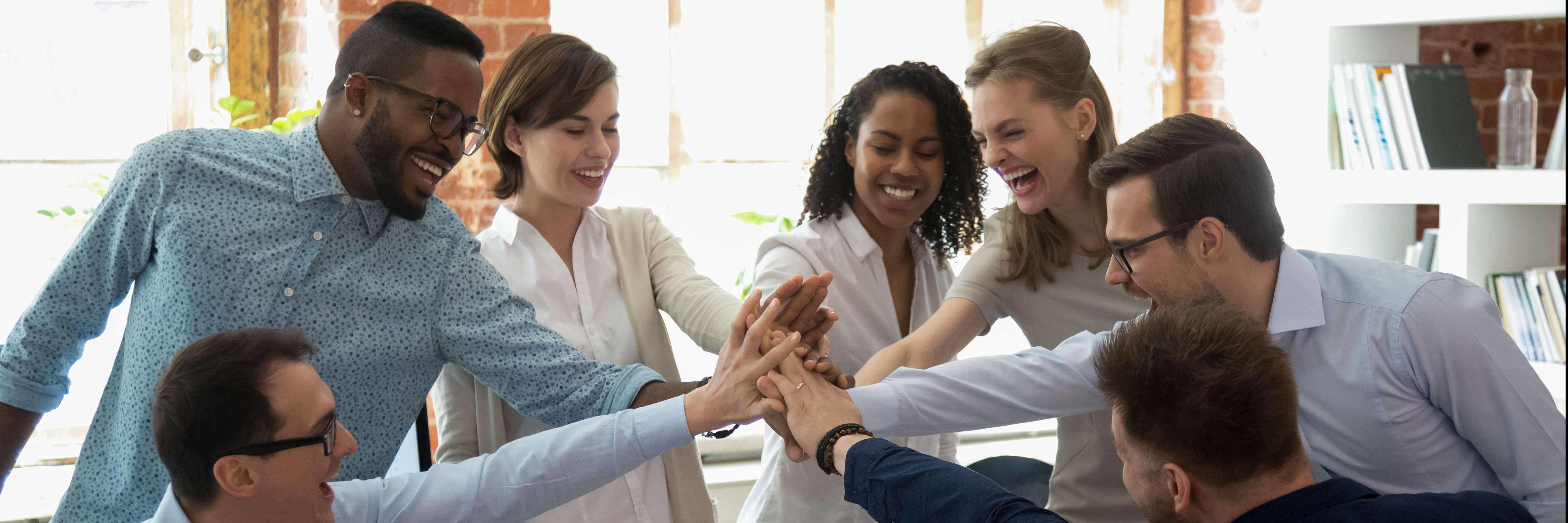 Colegas de trabalho em uma roda, unido as mãos ao centro e comemorando.