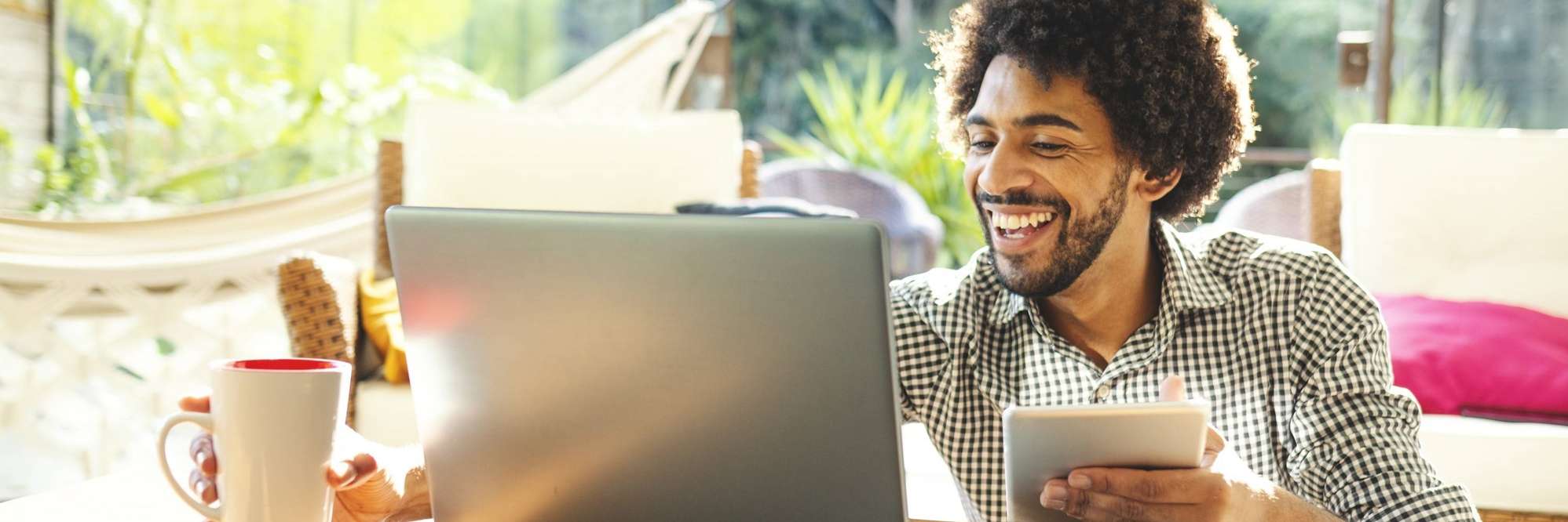 Homem segurando iapd e na frente do laptop sorrindo.