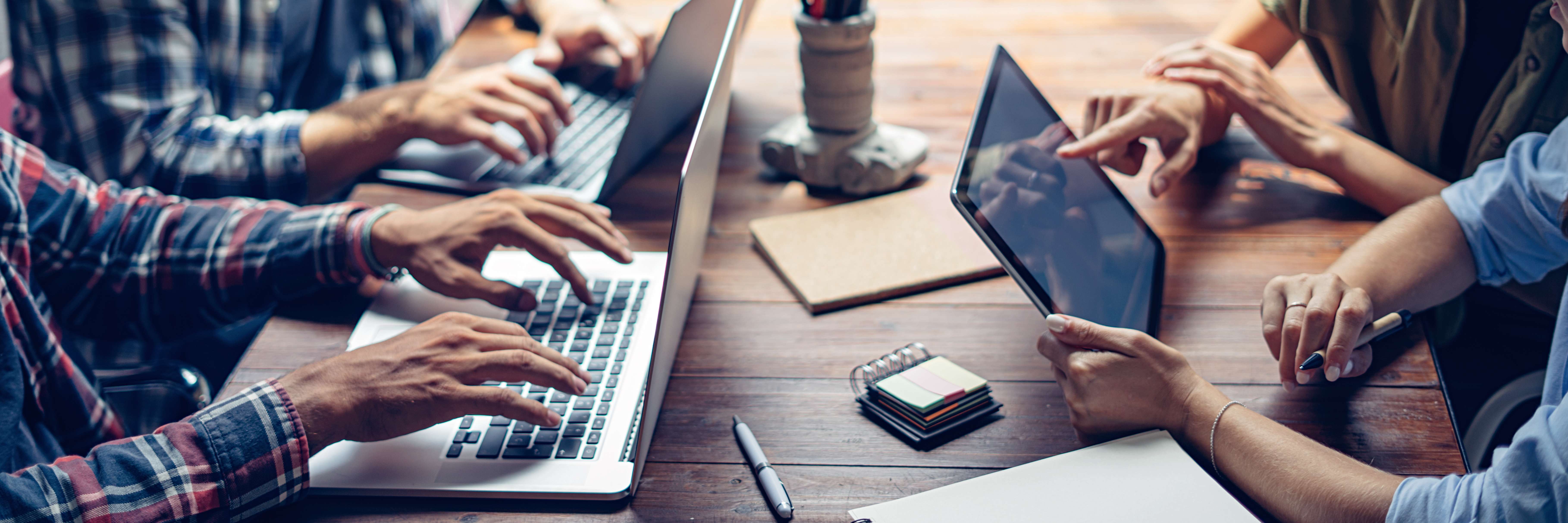 Pessoas em uma mesa de reunião, com notebooks e tablet.